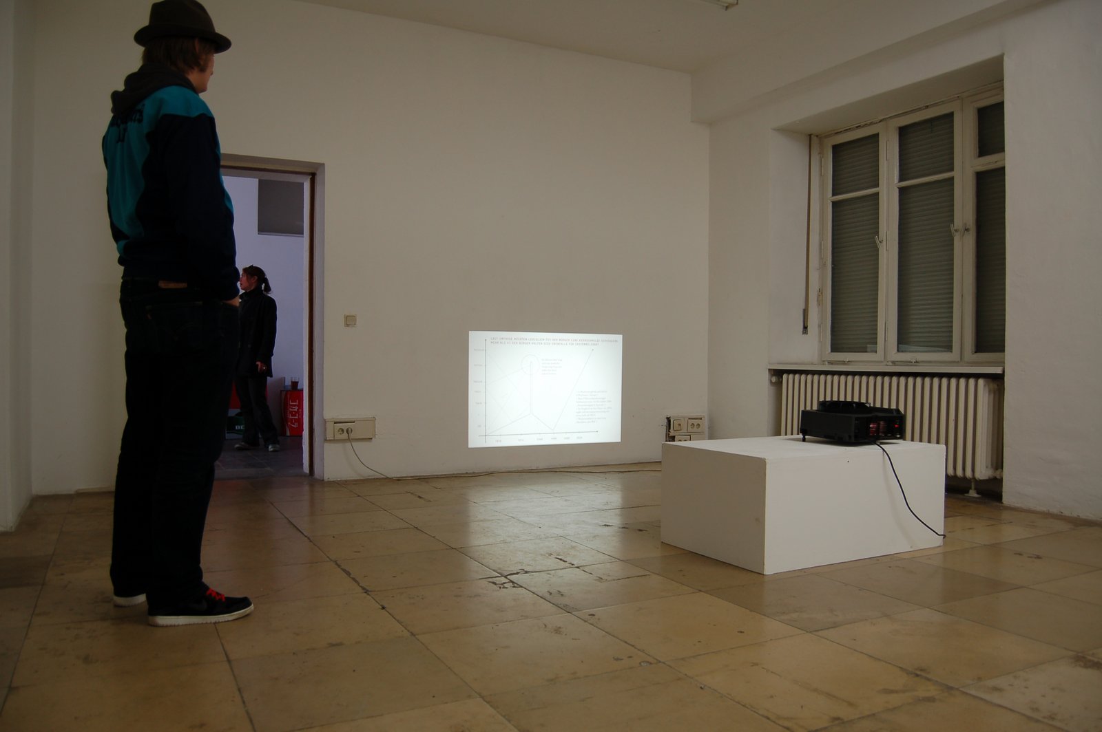A figure standing beside the projected chart in the white gallery space