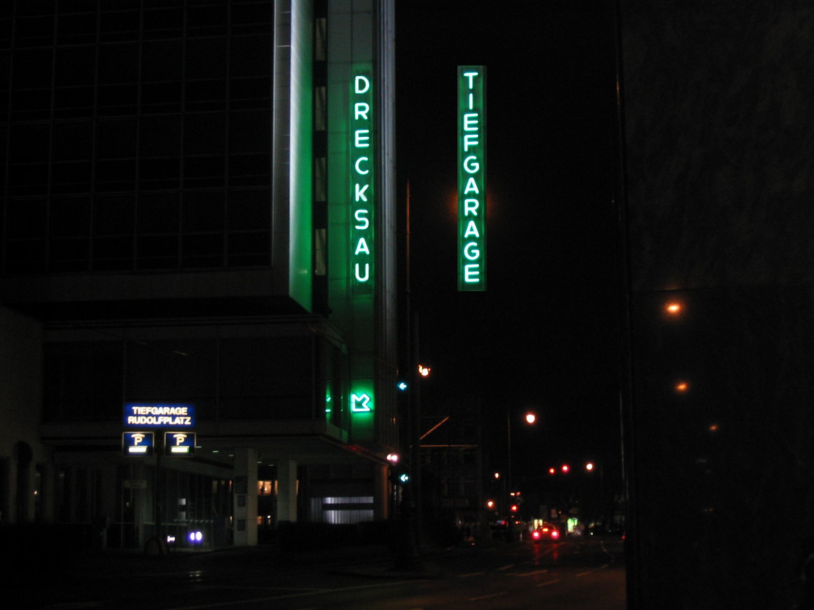 Cologne at night — green neon on a building reading DRECKSAU and VERSAGER